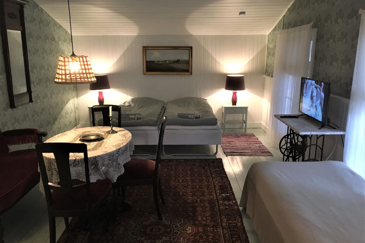 A bedroom with a bed, a TV, a table with a chair, and two lamps.