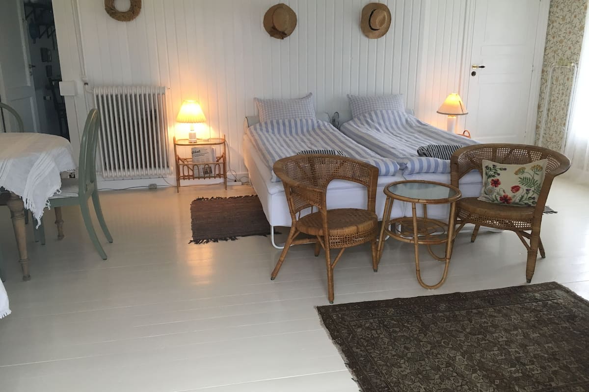 A room with a bed, two nightstands, a wicker chair, a small table, and a patterned rug.