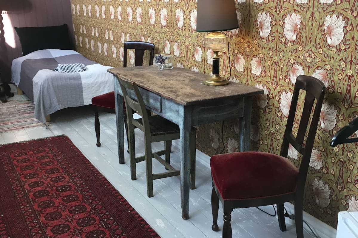 A room with a bed, a desk, a chair, a lamp, and a patterned wallpaper.