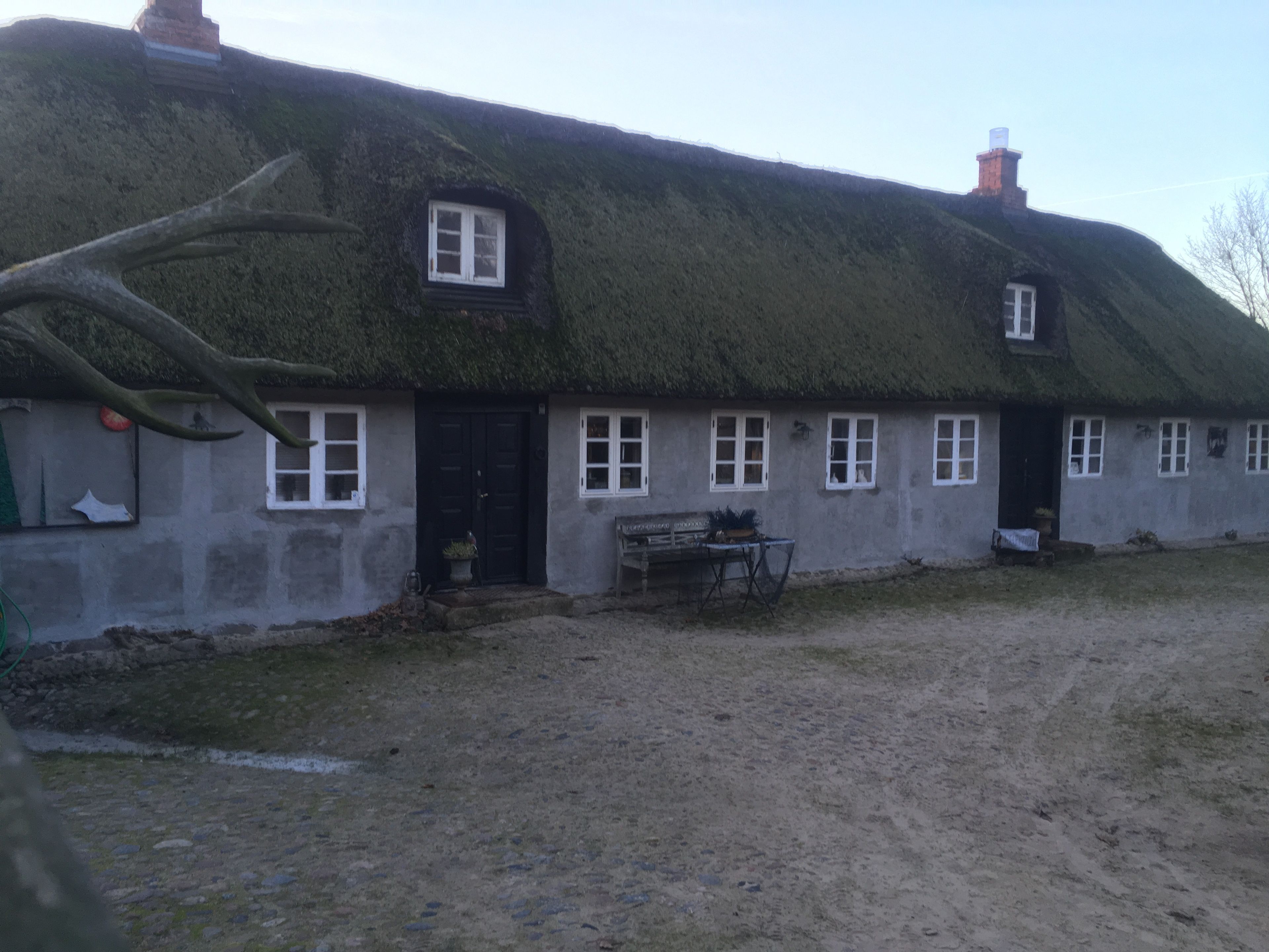 Et traditionelt bindingsværkshus med stråtækt tag, en lille veranda og en bænk.