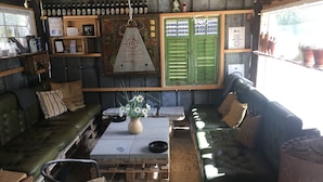 A rustic interior with a wooden table, leather sofas, and a variety of bottles on shelves. - Farm61 (Tjele)