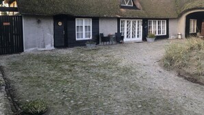 A traditional thatched-roof cottage with a gravel courtyard, a small seating area, and a gate labeled "RELAX". - Farm61 (Tjele)