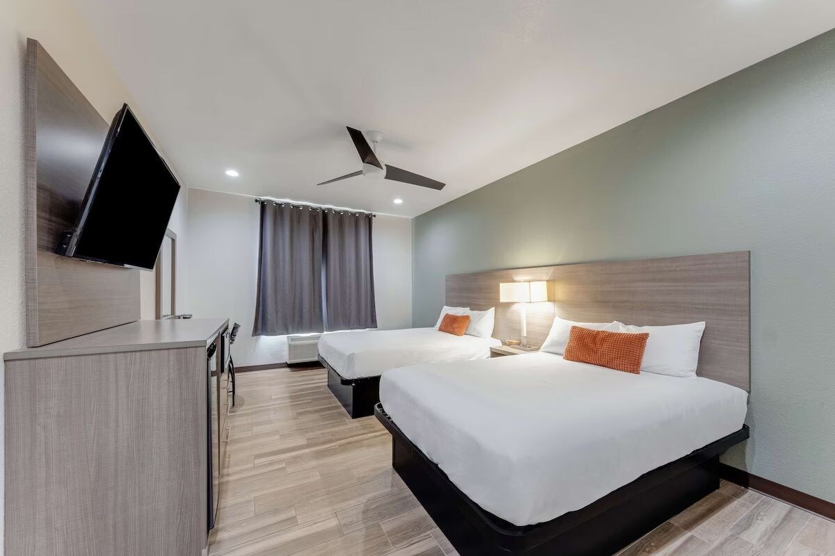 A hotel room with two beds, a TV, a ceiling fan, and a desk.