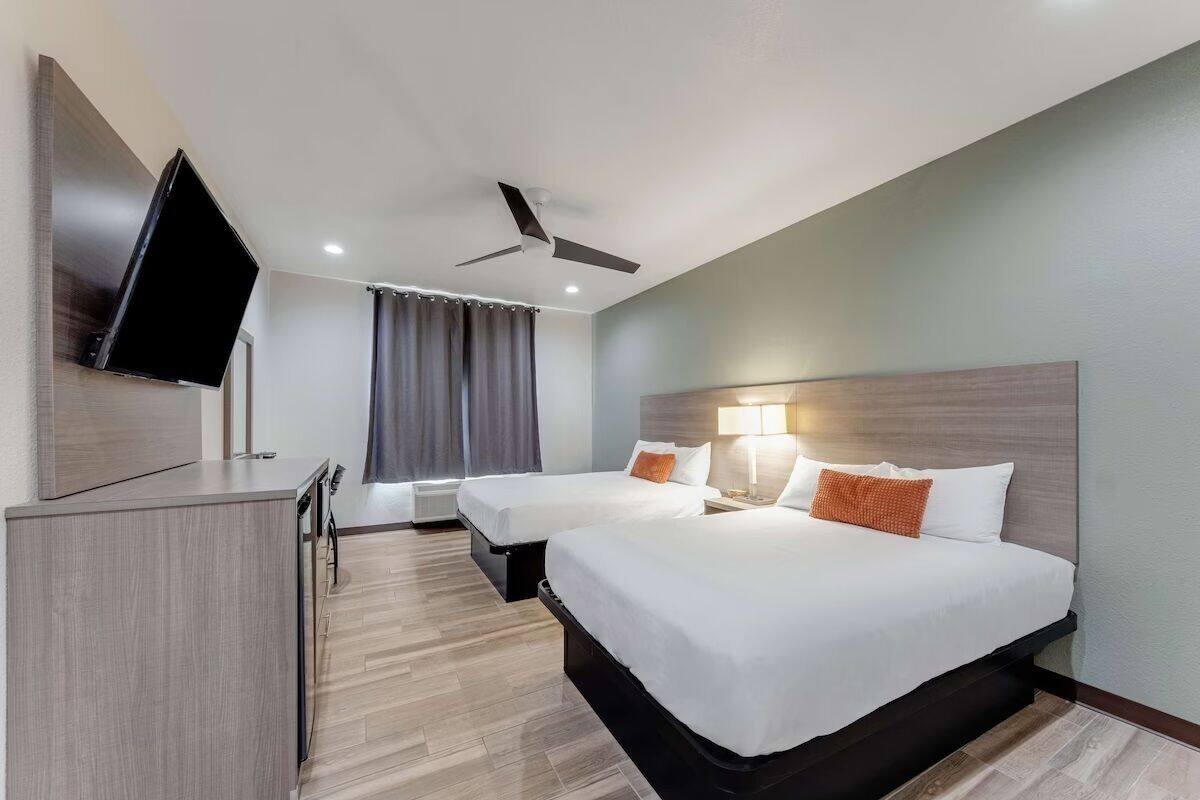 A hotel room with two beds, a TV, a ceiling fan, and a desk.