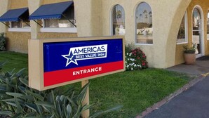 Ein Eingangsschild für Americabs Best Value Inn, das einen klaren Blick auf die Architektur des Gebäudes und einen gepflegten Rasen zeigt.
