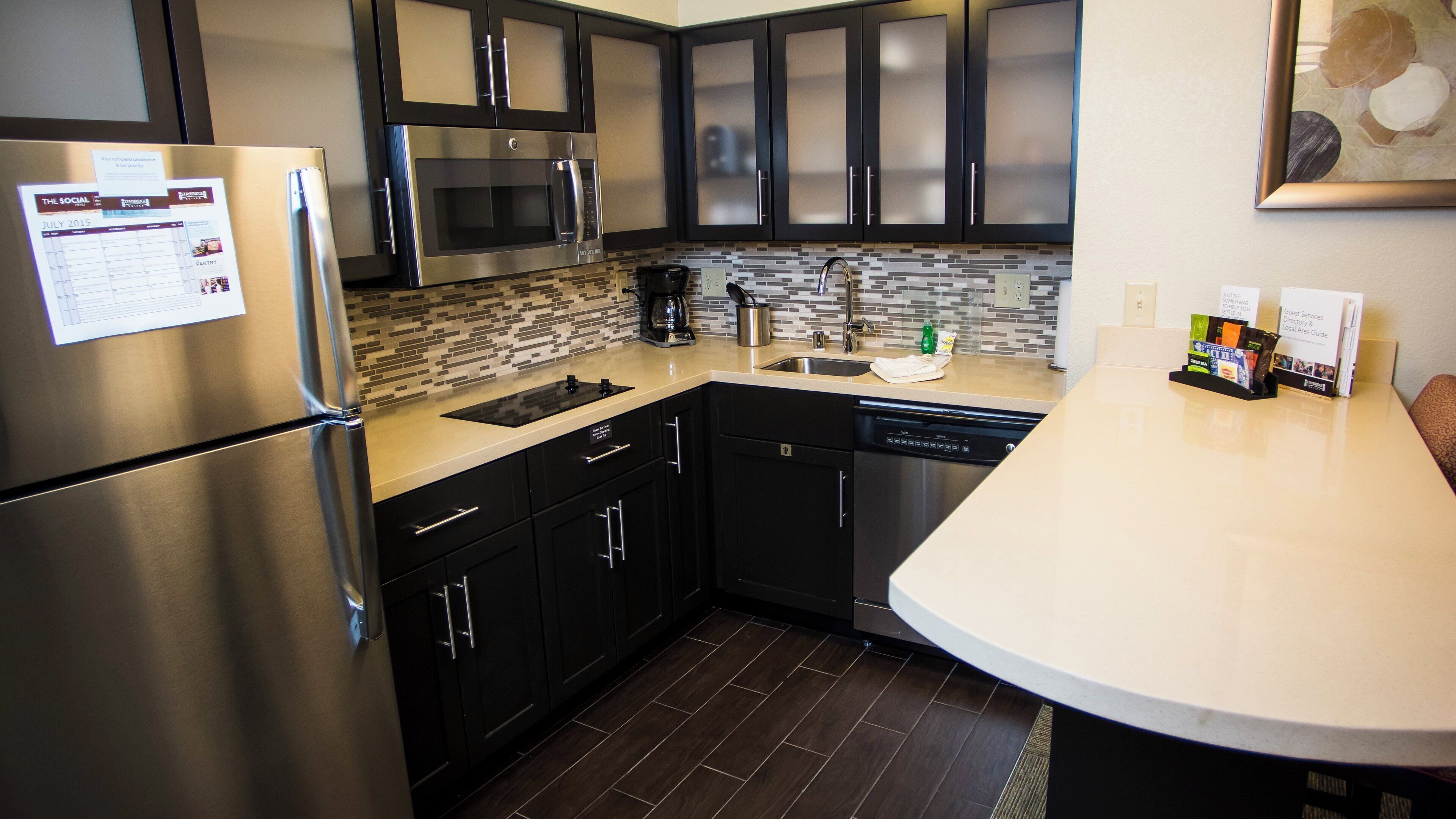 A modern kitchen with stainless steel appliances, dark cabinetry, and a tiled backsplash.