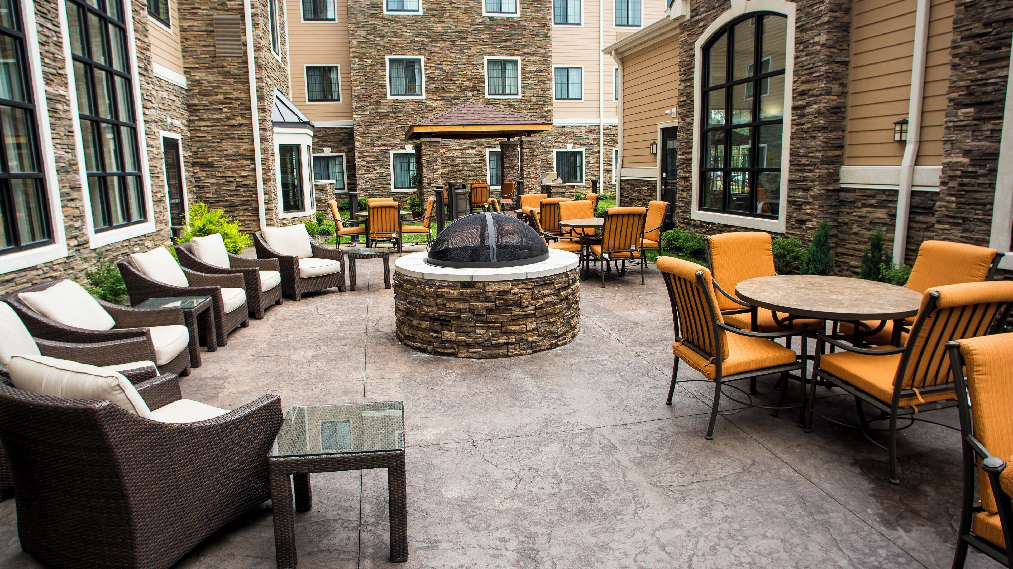 An outdoor patio area with wicker furniture, a stone fire pit, and a covered seating area.
