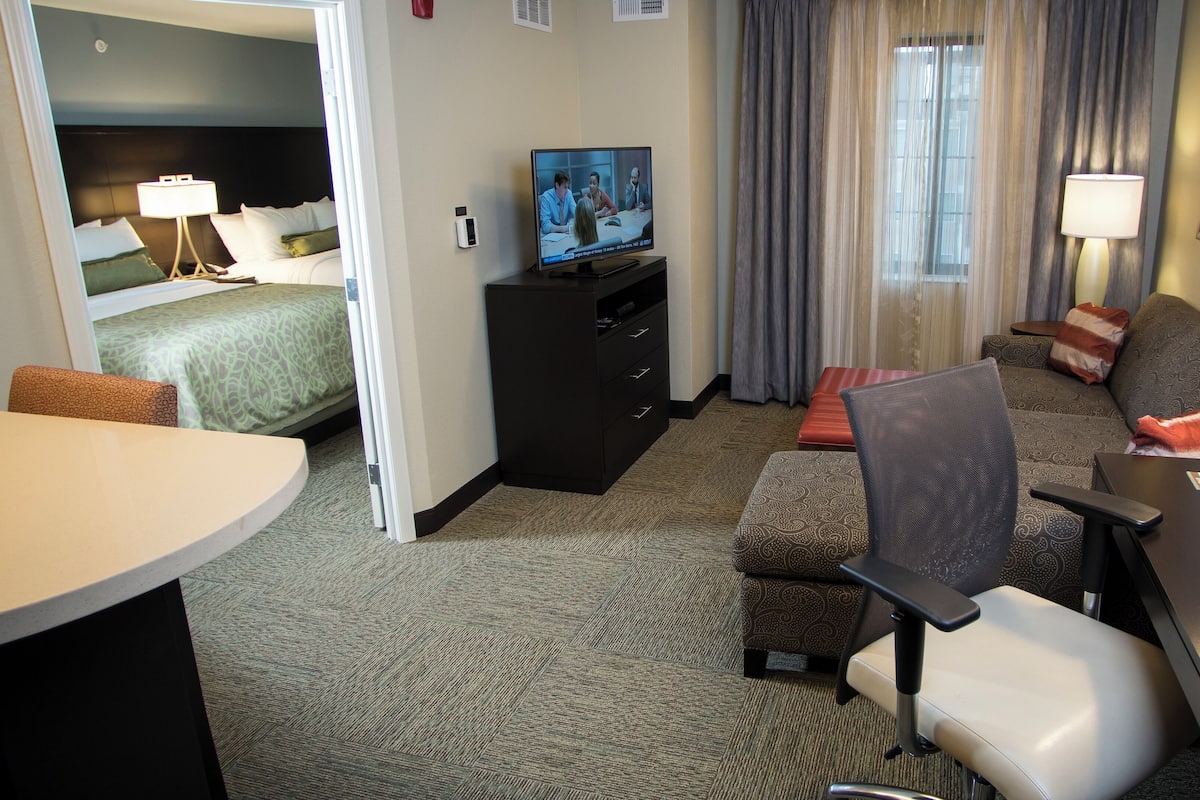 A hotel room with a bed, a TV, a desk with a chair, a sofa, and a small table.