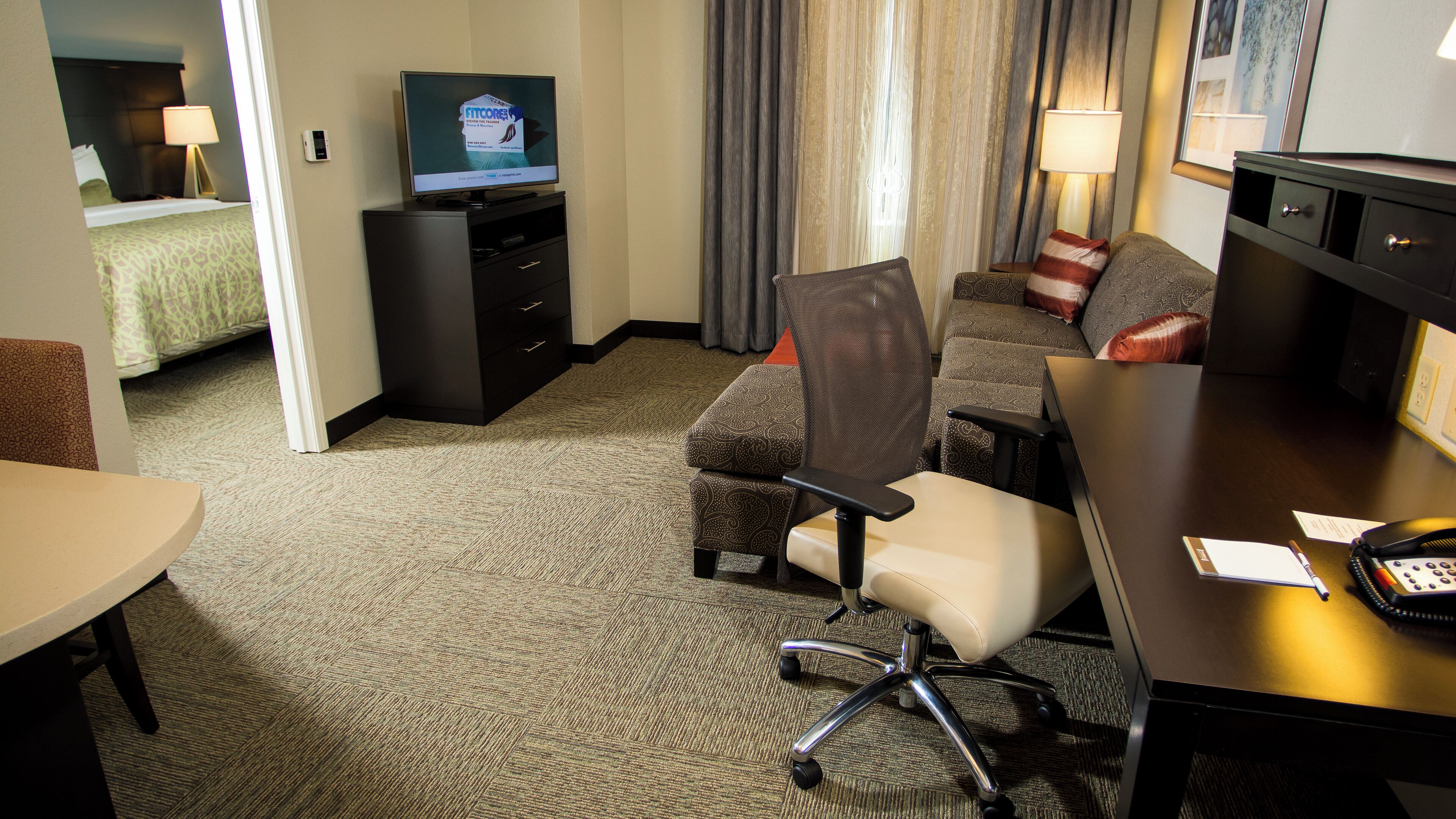 A hotel room with a bed, a TV on a stand, a desk with a phone, and a chair.