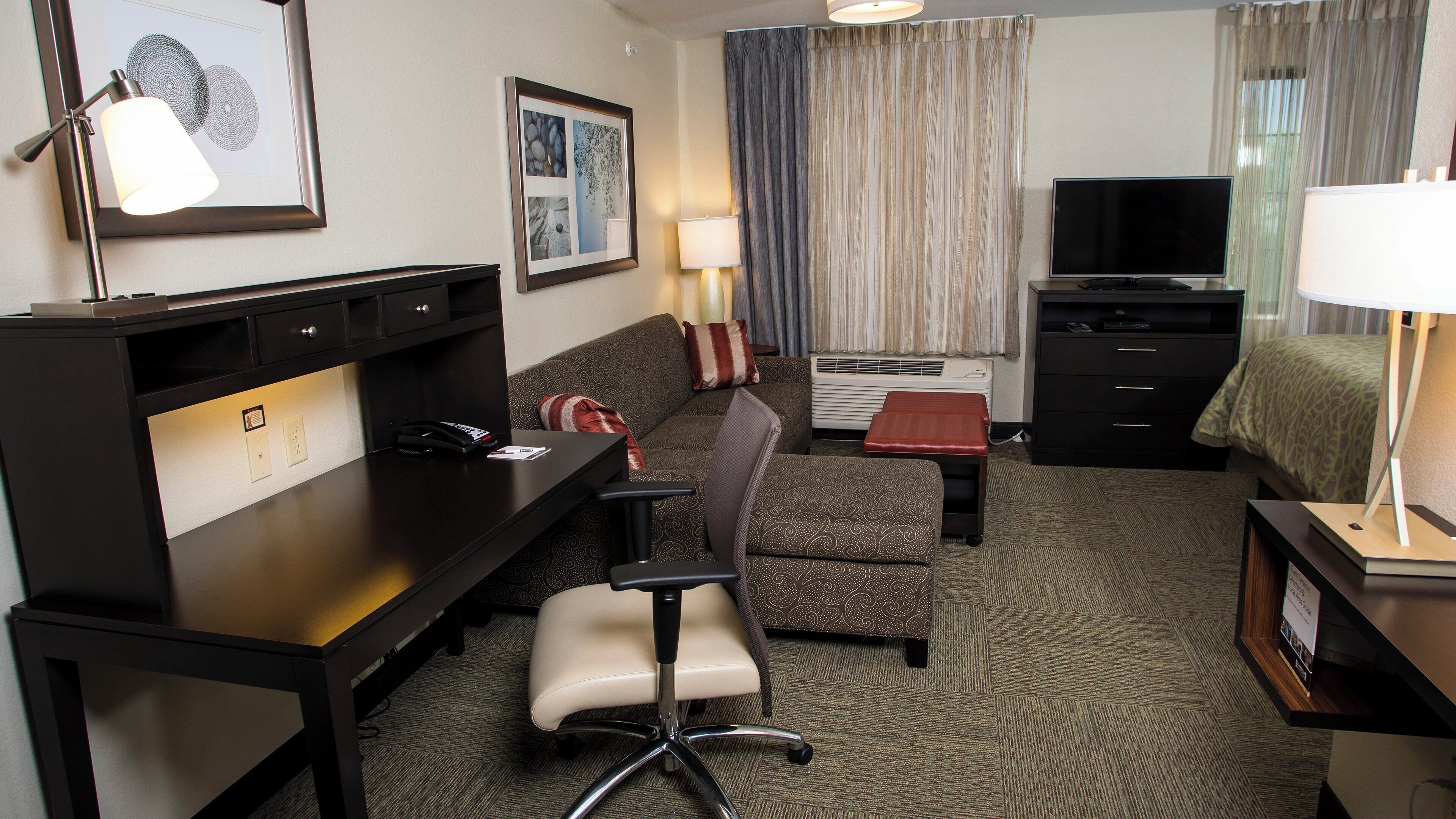 Ein Hotelzimmer mit Schreibtisch, Stuhl, Sofa, Fernseher und einem Bett.