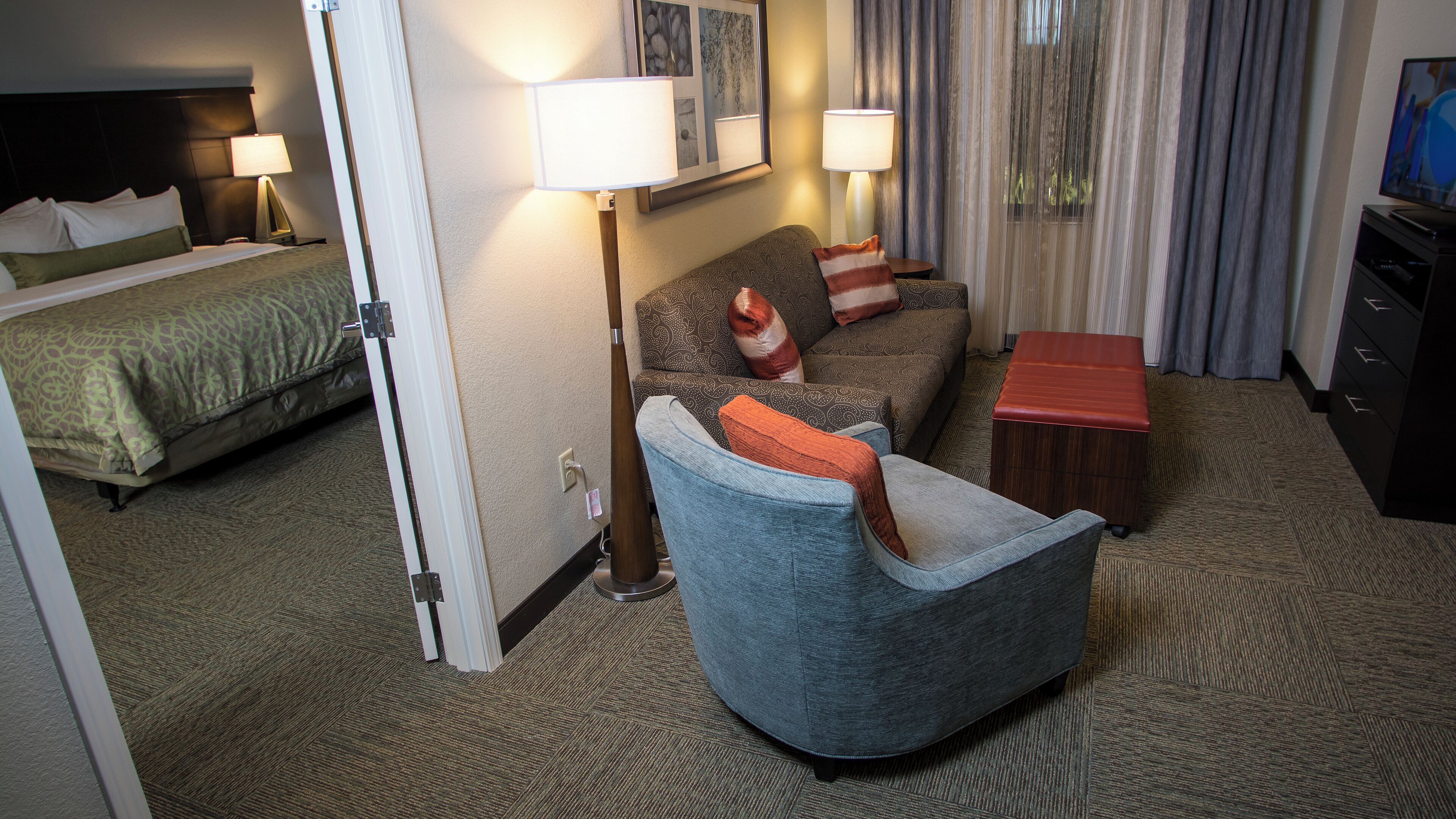 Une chambre d’hôtel avec un lit, un canapé, une chaise, une petite table et un téléviseur.
