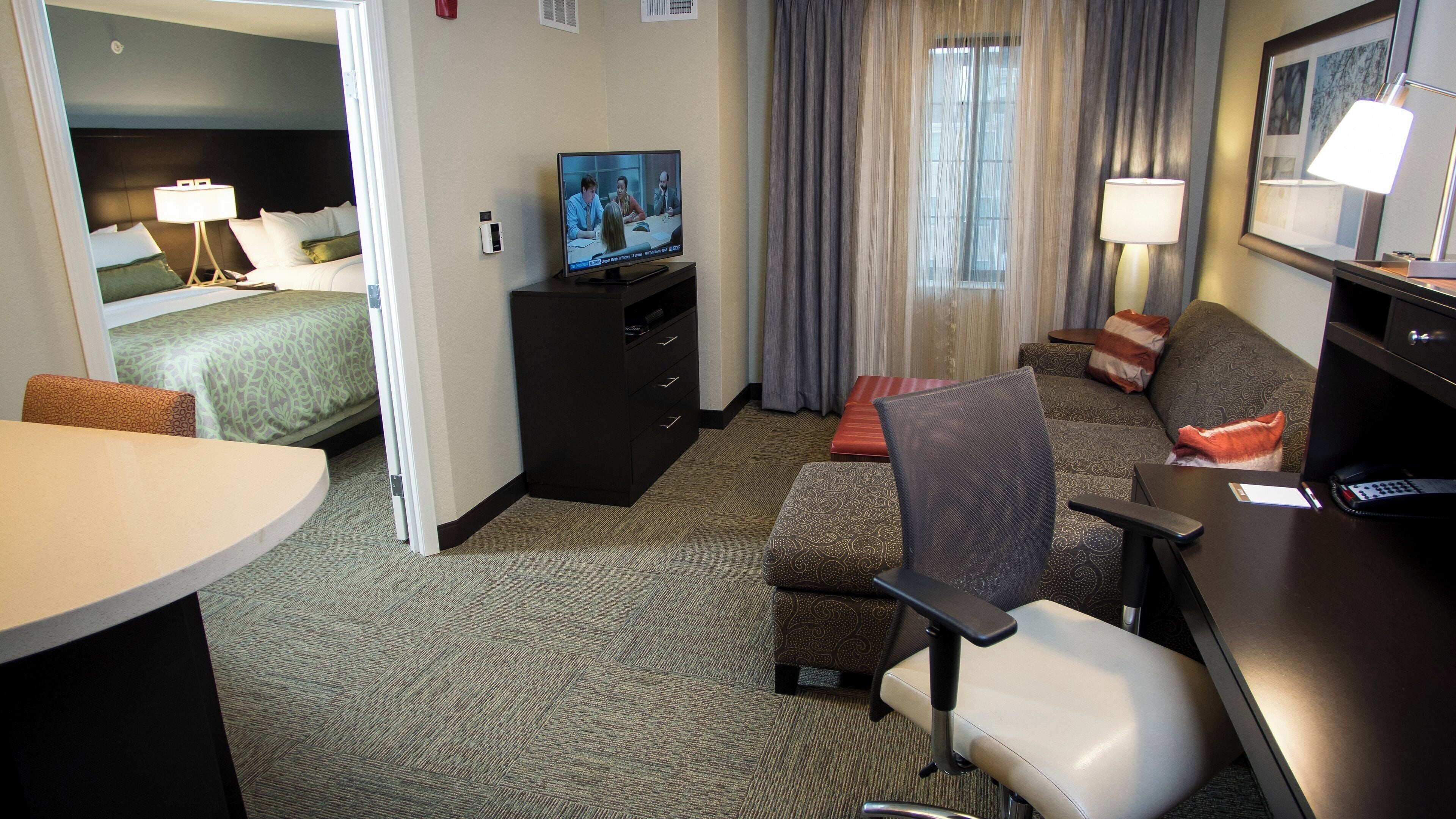 Une chambre d’hôtel comprenant un lit, un bureau avec un ordinateur, une télévision, un canapé et un fauteuil.