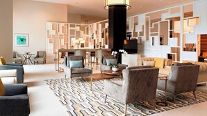 A modern hotel lobby with a central seating area, a large decorative pillar, and a patterned rug. - Sheraton McKinney Hotel (McKinney)