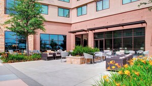 A modern building with a patio area featuring outdoor seating and a large window overlooking the interior. - Sheraton McKinney Hotel (McKinney)