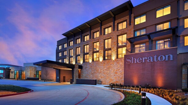 A Sheraton hotel with a stone facade, multiple windows, and a well-lit entrance. - Sheraton McKinney Hotel (McKinney)