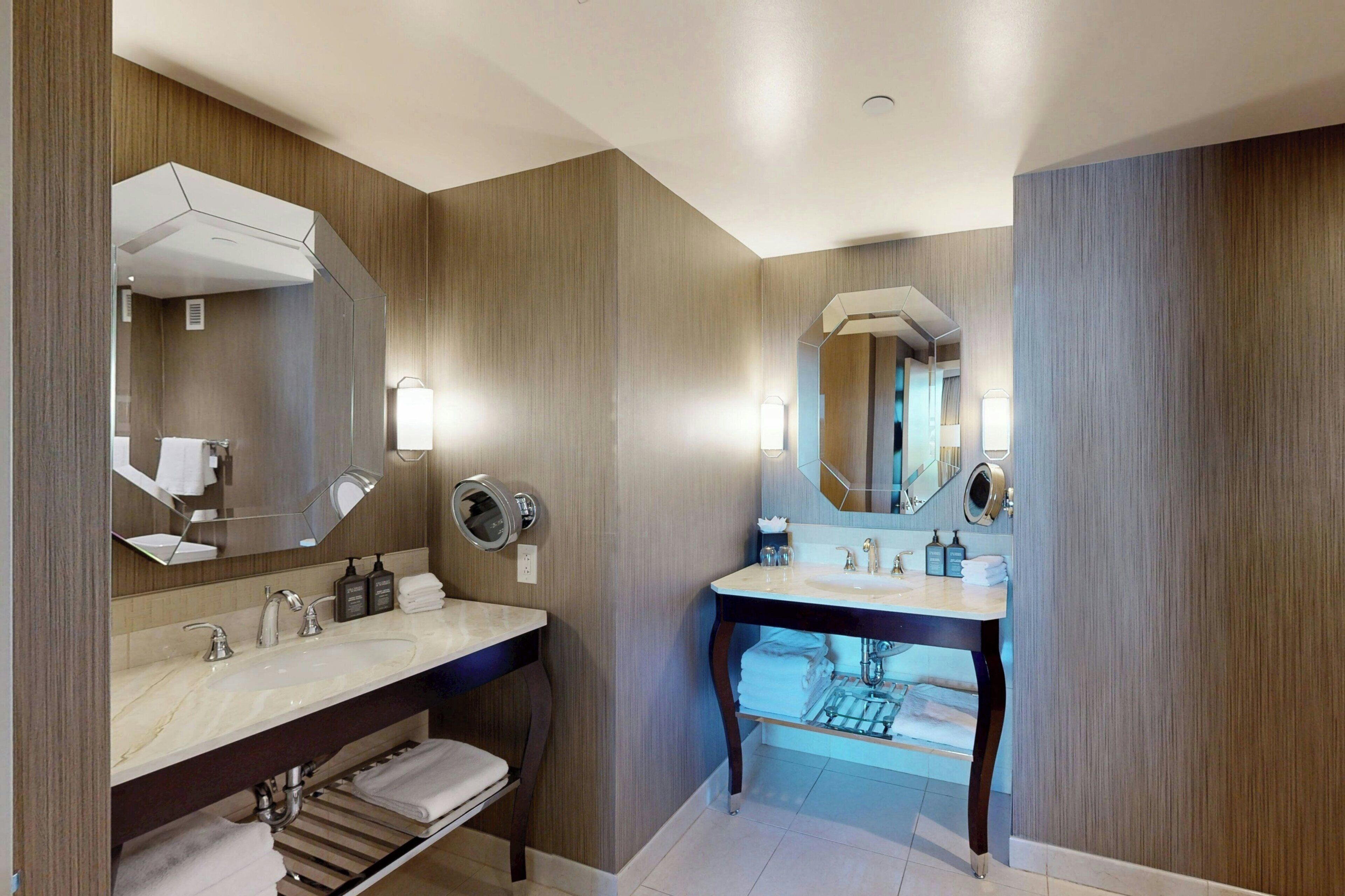 A modern bathroom with two sinks, a large mirror, and a vanity with a towel rack.
