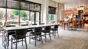 A modern dining area with a long table and chairs, large windows, and a view of the outside. - Sheraton McKinney Hotel (McKinney)