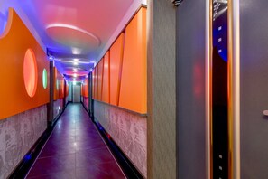 A brightly lit hallway with orange walls and a marble floor, leading to a door with a digital display. - Thebay Hotel (Busan)