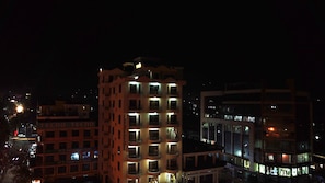 A multi-story building with balconies and lit windows, surrounded by other buildings. - Natron Palace Hotel (Arusha)