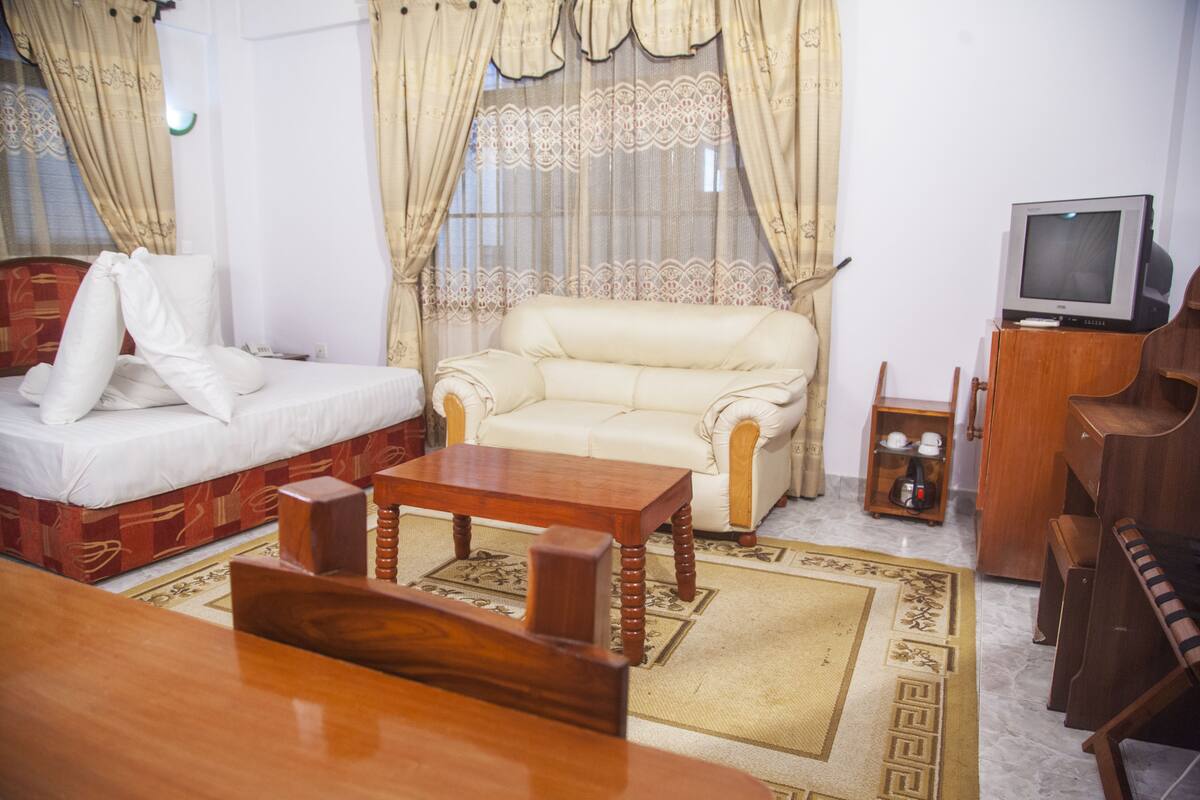 Una habitación con cama, sofá, una mesa de centro de madera, televisor y un armario.