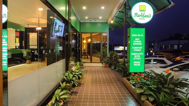 The exterior of Parkland Hotel with a green facade, a signboard listing amenities like free Wi-Fi, not power shower, comfort linens, simplicity with styles, and great value. - Parkland Hotel (Brinchang)
