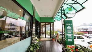 The exterior of Parkland Hotel with a green facade, a glass entrance, and a sign listing amenities like free Wi-Fi and hot showers. - Parkland Hotel (Brinchang)