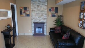 A living room with a fireplace, a black leather sofa, a small table, and abstract art on the walls.