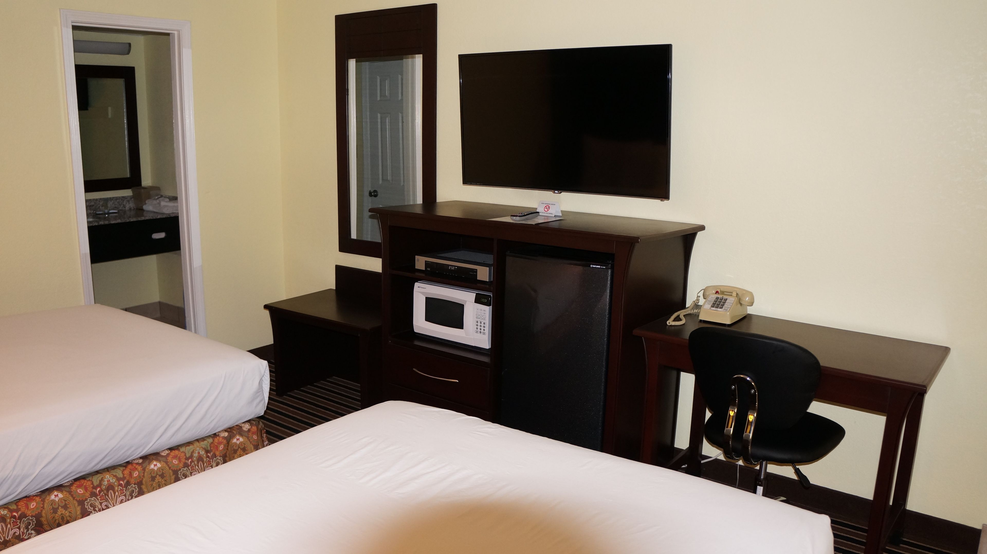 Habitación de hotel con dos camas, un escritorio, teléfono, microondas y televisión.