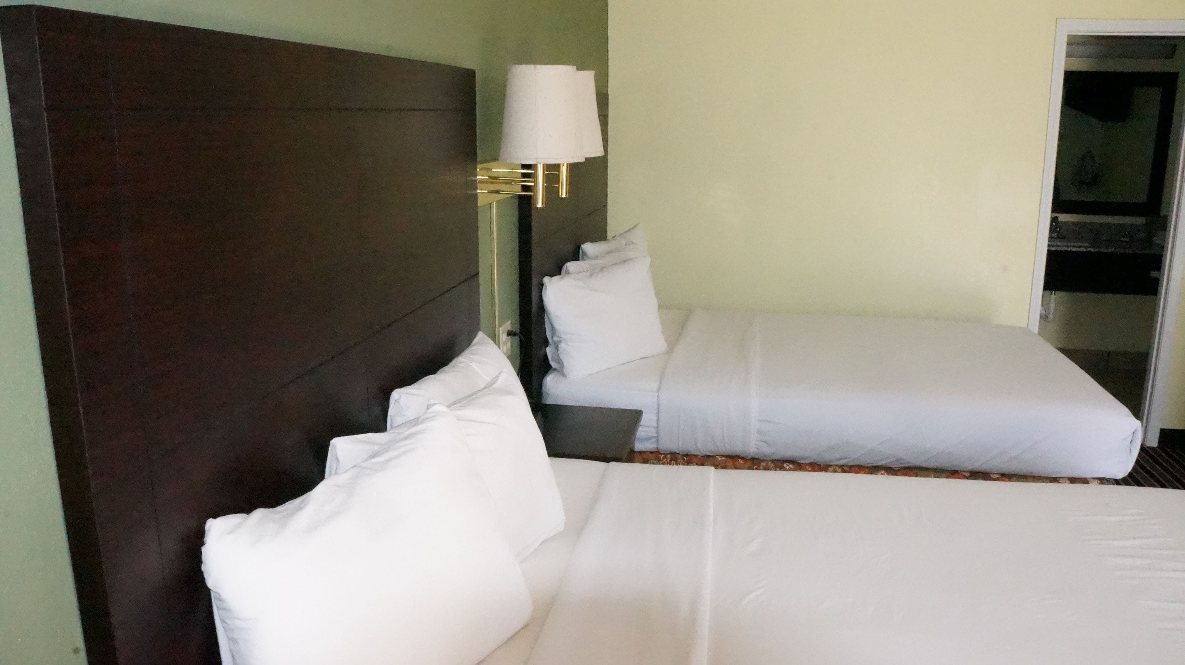 A hotel room with two beds, a dark wooden headboard, a wall-mounted lamp, and a door leading to a balcony.