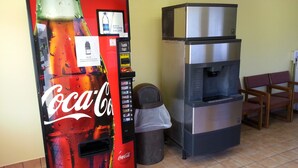 A Coca-Cola vending machine and a water dispenser in a room with tiled flooring and wooden chairs.