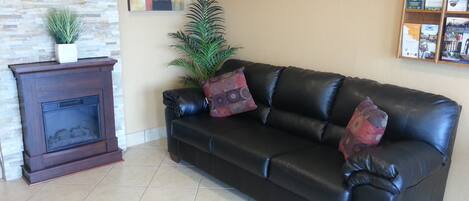 Un sofá de cuero negro con almohadones decorativos, una pequeña planta en maceta y una chimenea frente a una pared de piedra.