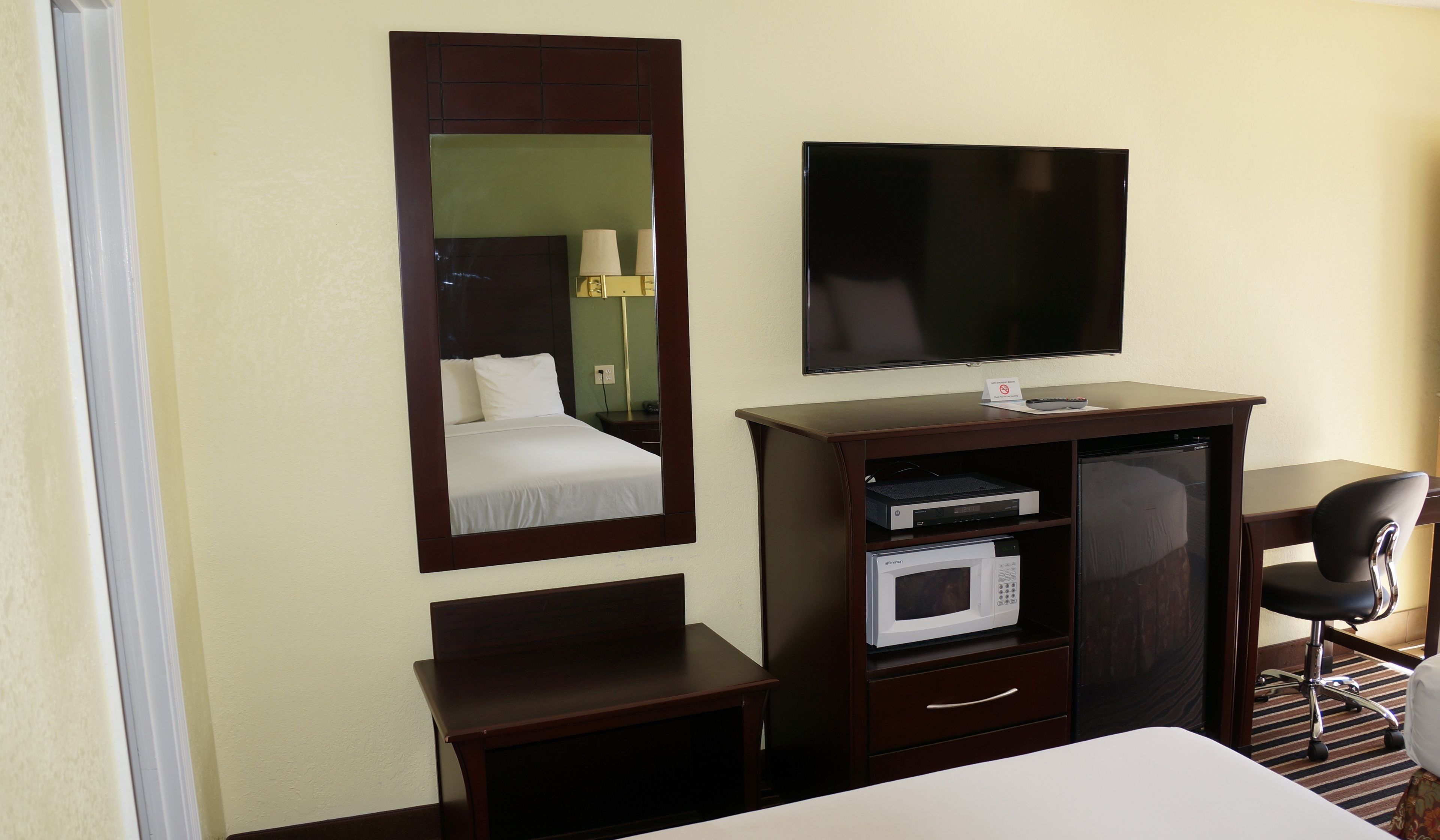 A hotel room with a bed, a TV, a desk with a computer, a microwave, and a chair.