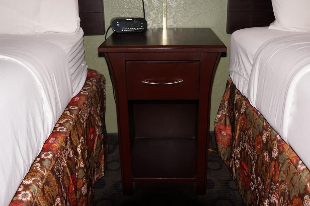 A hotel room with two beds, a nightstand with a clock, and a patterned bedspread.