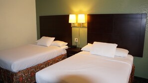 Habitación de hotel con dos camas individuales, una mesita de noche con lámpara, y una lámpara de pared.