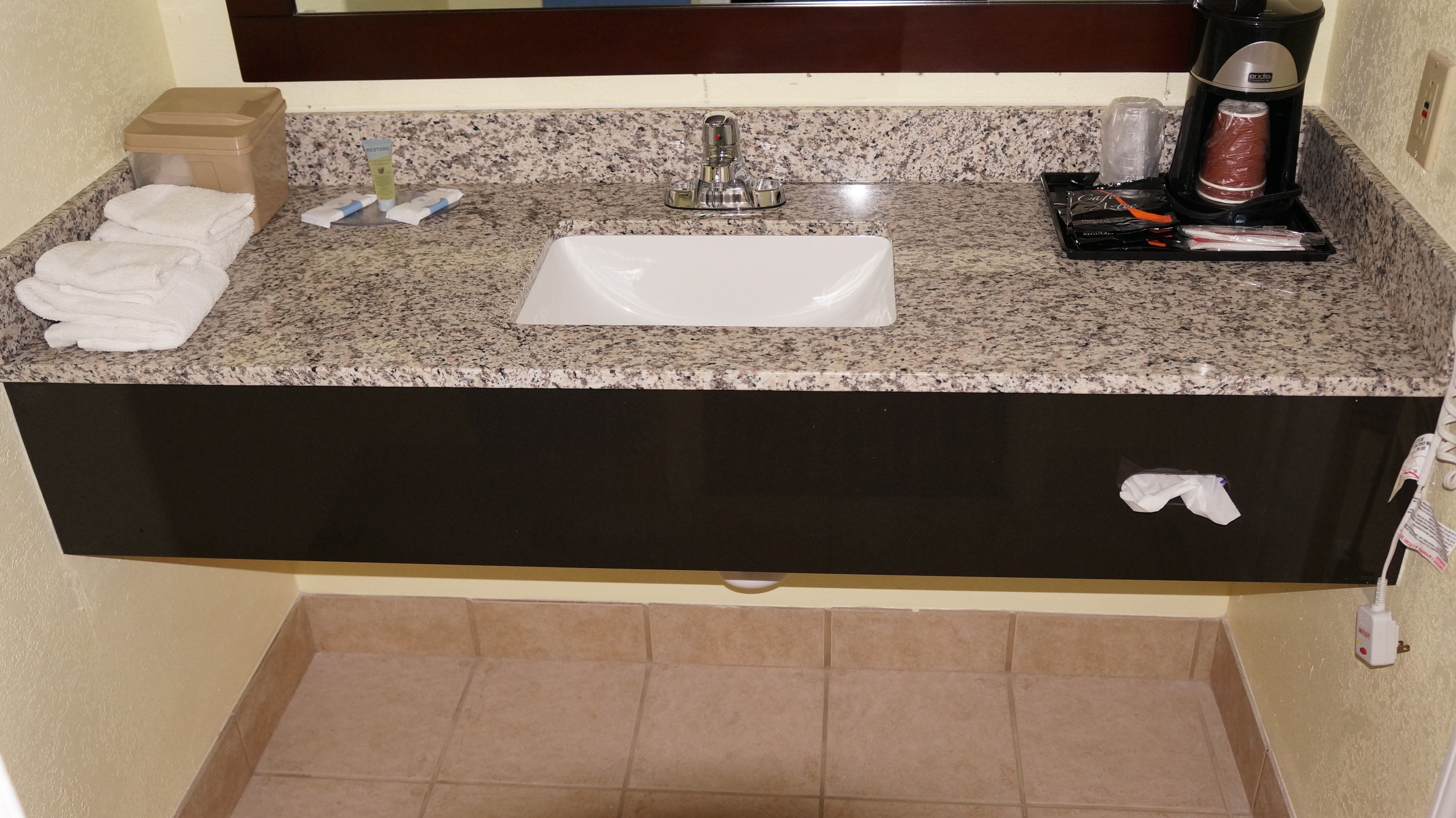 Ein Badezimmer mit Granitplatte, einem weißen Waschbecken, einer Kaffeemaschine und Toilettenartikeln.