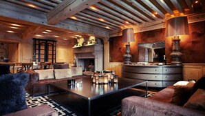 A spacious living area with a fireplace, wooden beams, and a large coffee table. - Le Saint Joseph (Courchevel)