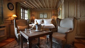 A traditional room with a wooden ceiling, a bed with white linens, two armchairs, a table with a bottle and glasses, and a fireplace. - Le Saint Joseph (Courchevel)