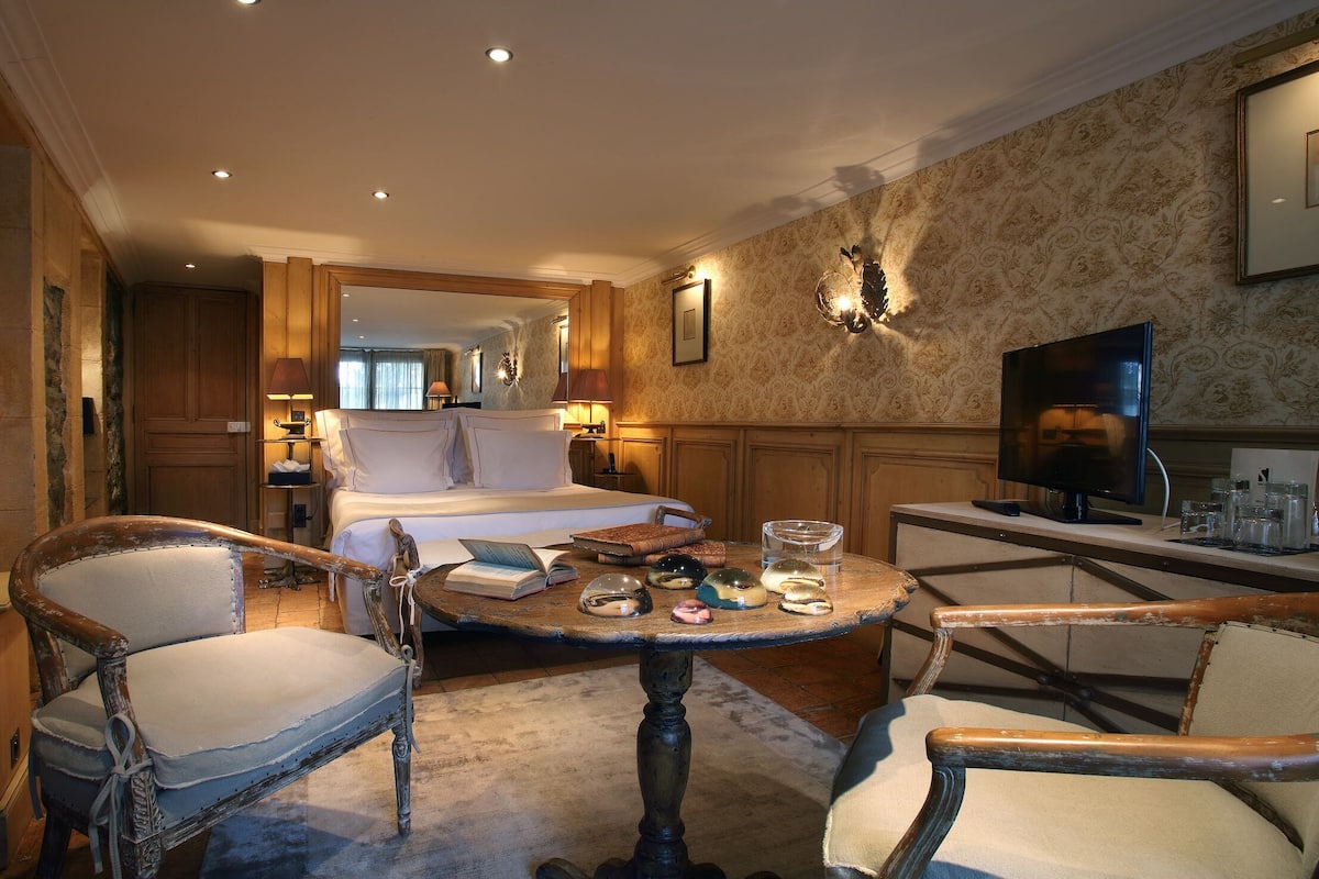 A hotel room with a bed, a desk, a television, and a dining table with chairs.