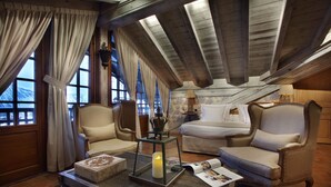 A cozy living room with a high ceiling, wooden beams, two armchairs, a sofa, a coffee table with a candle, and a magazine. - Le Saint Joseph (Courchevel)