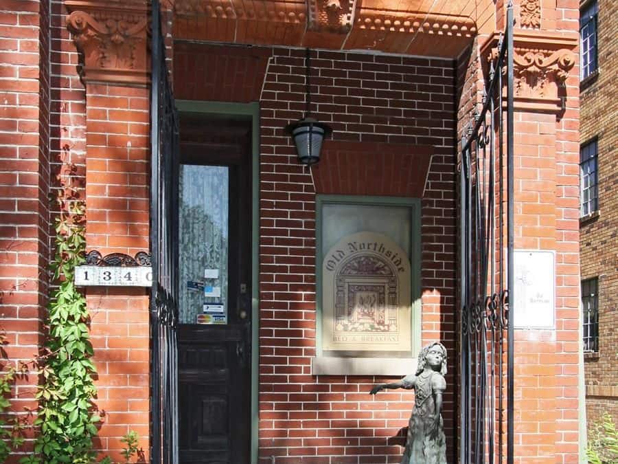 A brick building with a black door, a staircase leading to the entrance, and a plaque above the door.