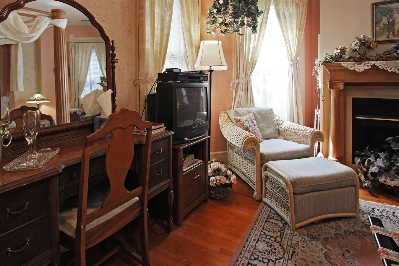 A traditional room with a wooden desk, a television, a wicker sofa, and a fireplace.