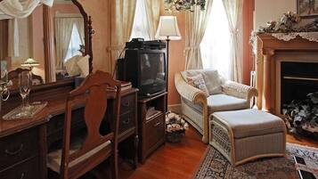 A traditional room with a wooden desk, a television, a wicker sofa, and a fireplace.