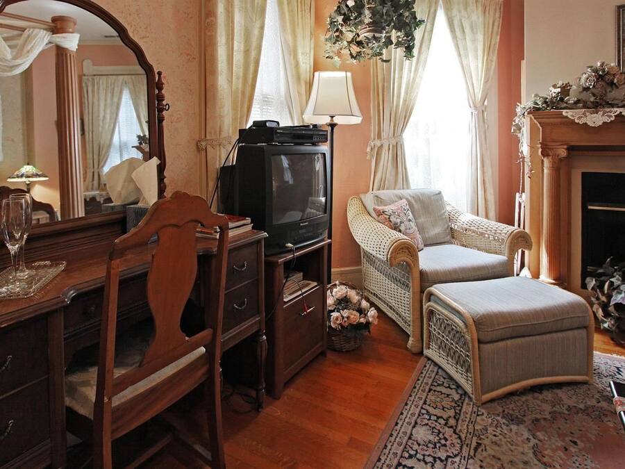 A traditional room with a wooden desk, a television, a wicker sofa, and a fireplace.