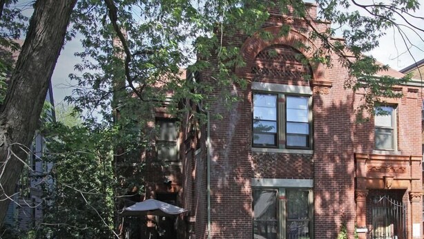 A two-story brick building with a small patio area and a covered seating space.
