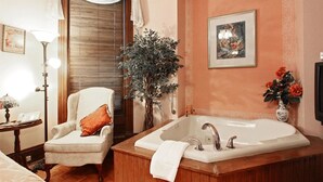 A bathroom with a large bathtub, a chair, a floor lamp, and a potted plant.