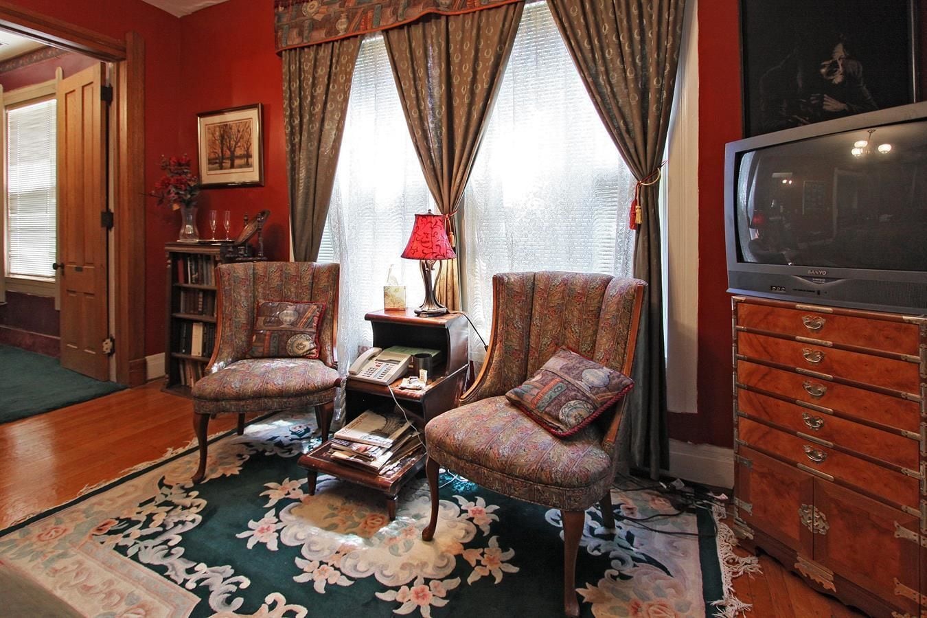 Una sala de estar acogedora con dos sillones estampados, una mesita con lámpara, una estantería y un televisor sobre un mueble de madera.