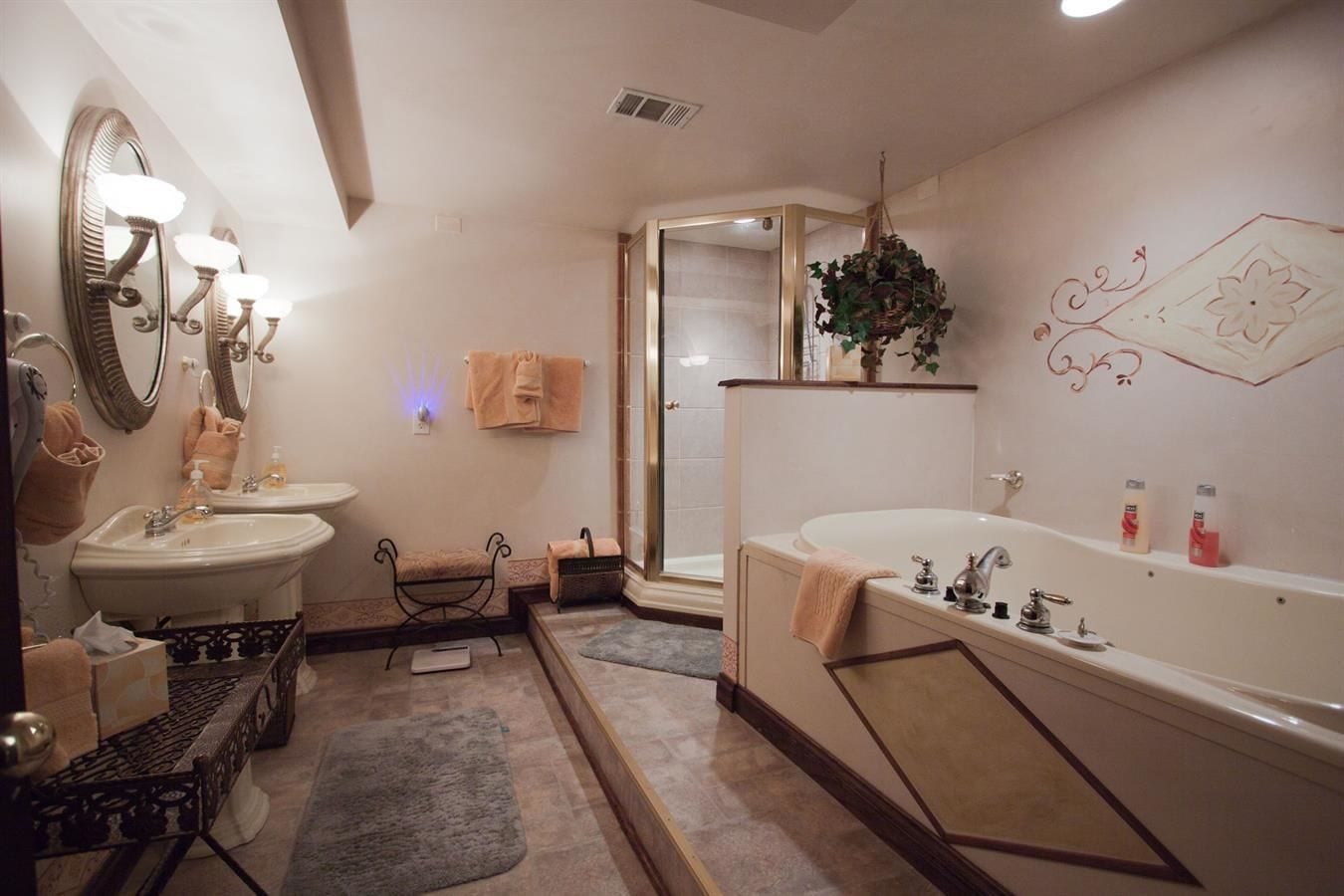 Une salle de bain avec une grande baignoire, deux lavabos, un miroir avec éclairage intégré, un porte-serviettes et un espace douche.