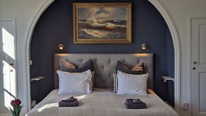 A bedroom with a large bed, two bedside tables, a nightstand, a painting above the bed, and a window on the left. - Brunsbo G:a Biskopsgård Hotell & Konferens (Skara)