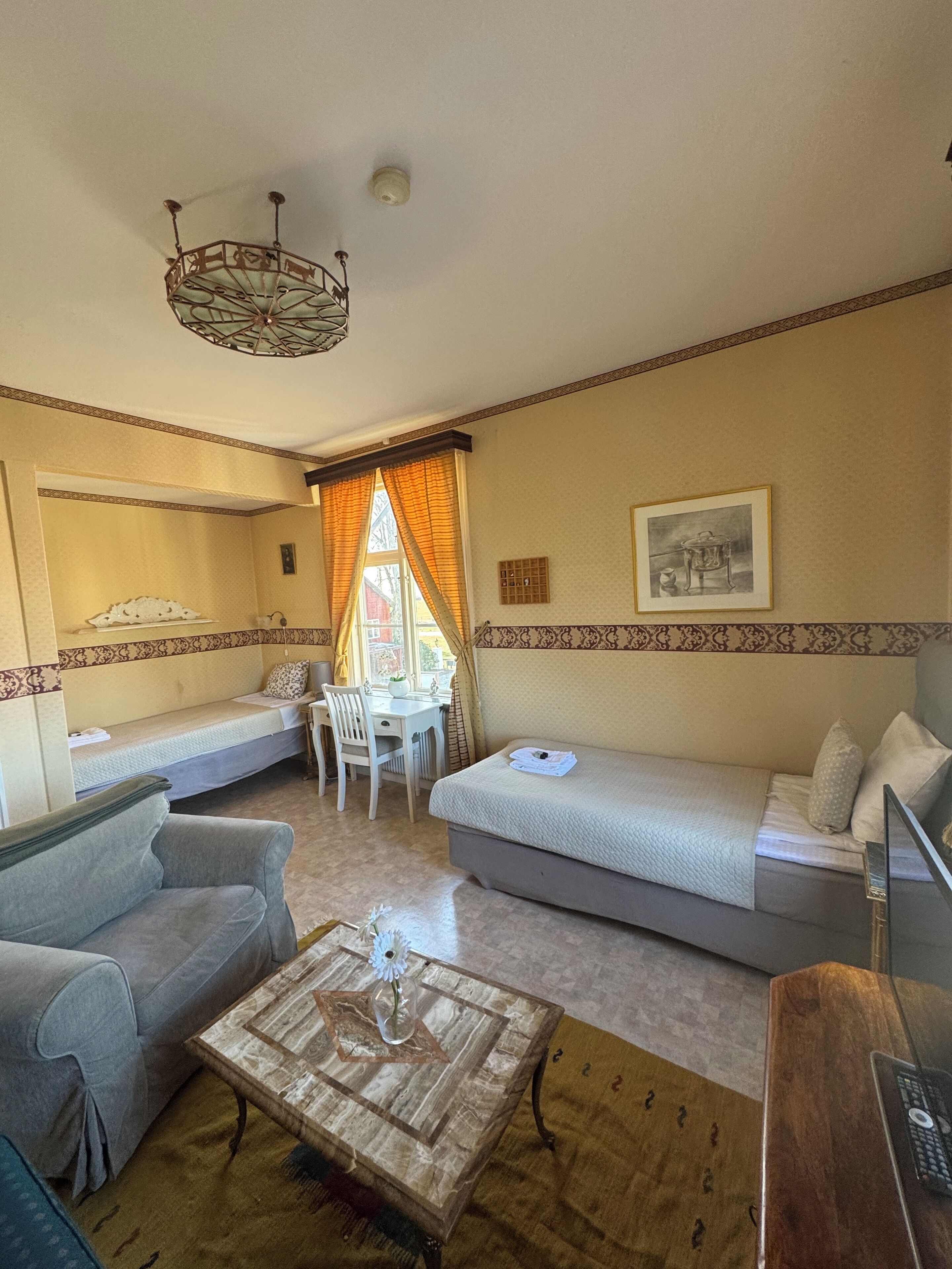 A cozy room with a sofa, a small table with a vase, a desk, and a bed.