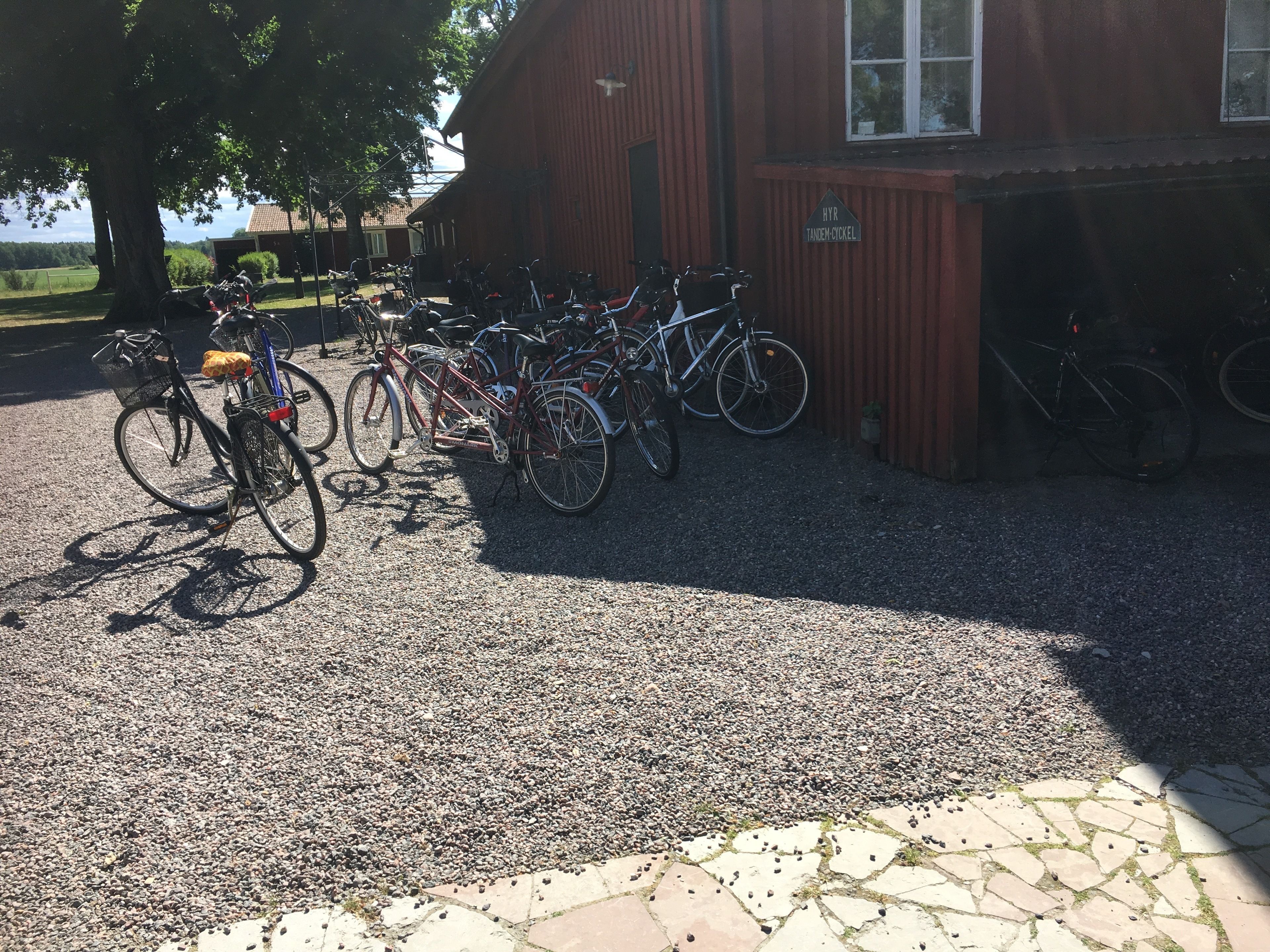 Un'area di parcheggio sterrata con biciclette parcheggiate di fronte a un edificio rosso con un cartello che riporta la scritta "HVR TANDEM-CICKEL".